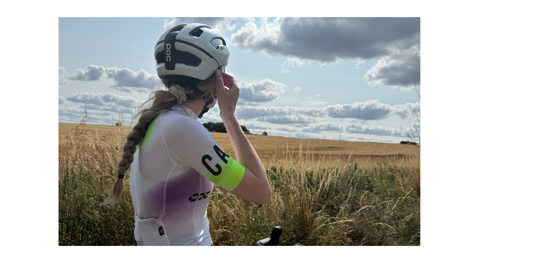 Woman cyclist stopped on a sunny, cloudy day to look out at the landscape of fields in the British countryside. 