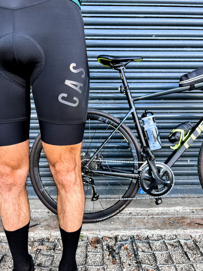 Men's black detachable magnetic buckle sleek bib shorts with reflective detail. CAS Feel the Freedom colourful reflective logo. Outdoors image. Cube bike. 